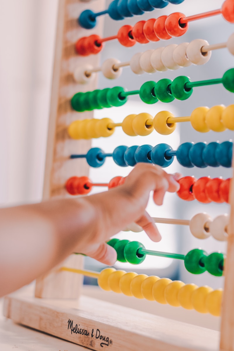 Un jeune enfant concentré manipulant activement un boulier Montessori, explorant et apprenant les concepts de base de la numération et de l'arithmétique grâce à ce matériel pédagogique coloré."