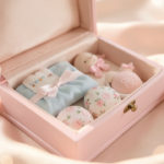 Coffret de naissance élégant avec des objets souvenirs délicats disposés sur un tissu doux, éclairage lumineux et ambiance pastel.